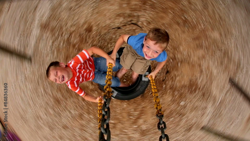 Two young boys spinning tire swing at school playground