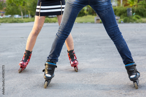 Bodies of two female skaters. Diverse dressed legs of two slim girls skating on roller skates on paved road together 