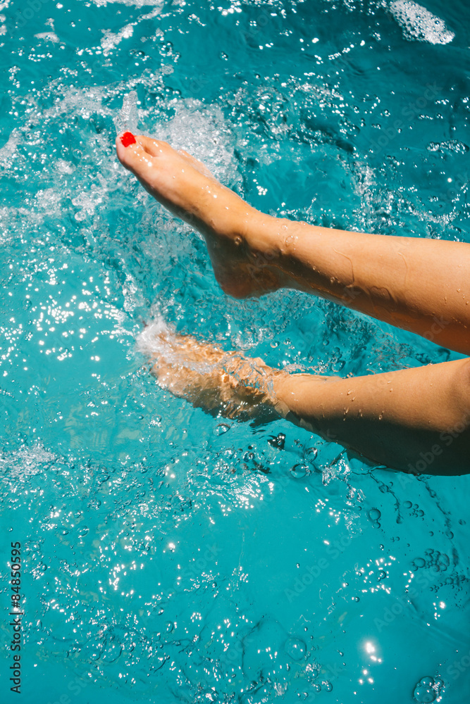 Legs in the water of a woman sitting on the edge of a swimming p