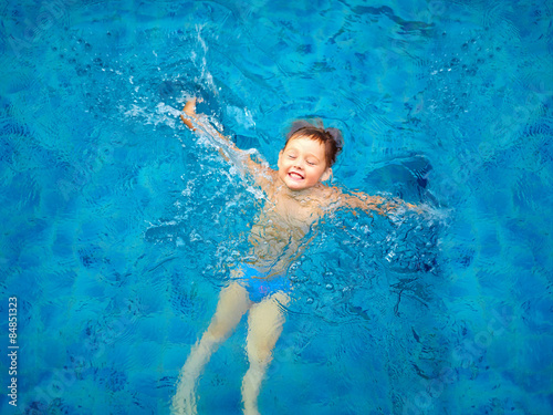 cute kid, boy swimming in pool water, top view