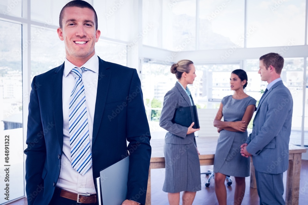 Fototapeta premium Businessman smiling at camera with colleagues behind him