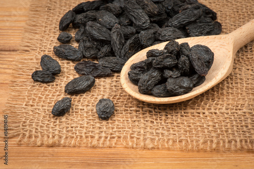 Black raisins on the wooden background.