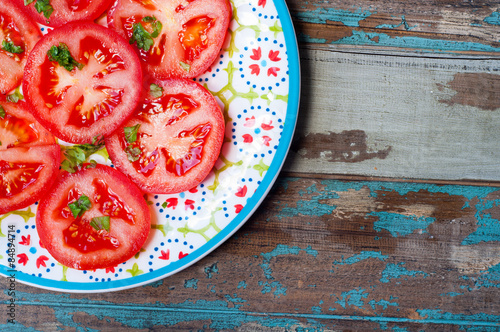 Sliced fresh tomatoes garnished with olive oil, parsley and basil served on a rustic wooden table. 