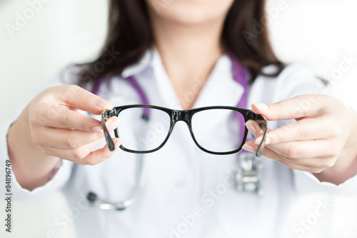 Female oculist doctor's hands giving a pair of black glasses