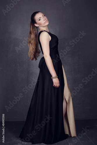 Young brunette lady in black ang golden dress posing on grey background
