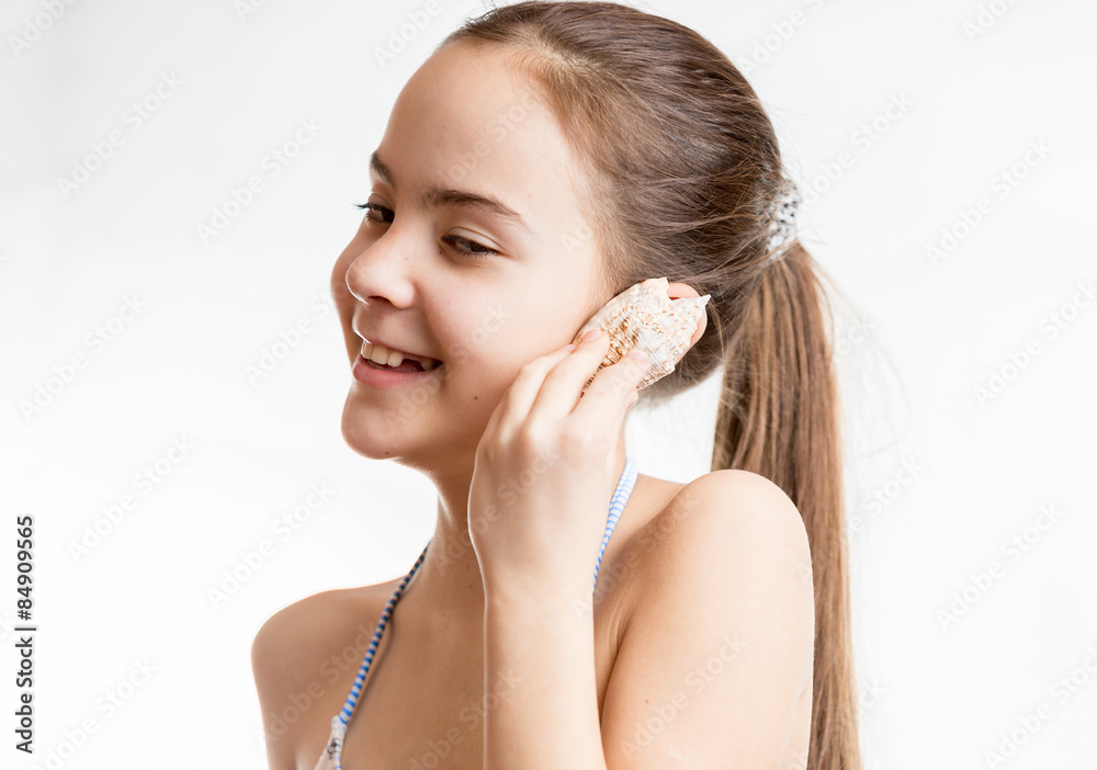 smiling girl holding seashell next to ear and listening to ocean smiling girl holding seashell next to ear and listening to ocean