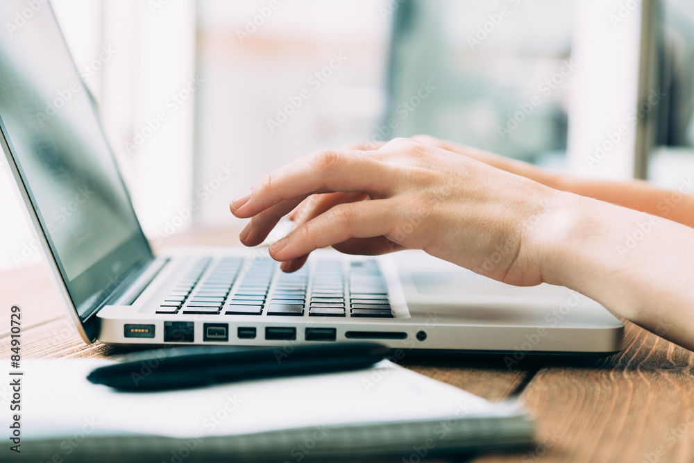 Woman working with laptop placed on wooden desk Woman working with laptop placed on wooden desk