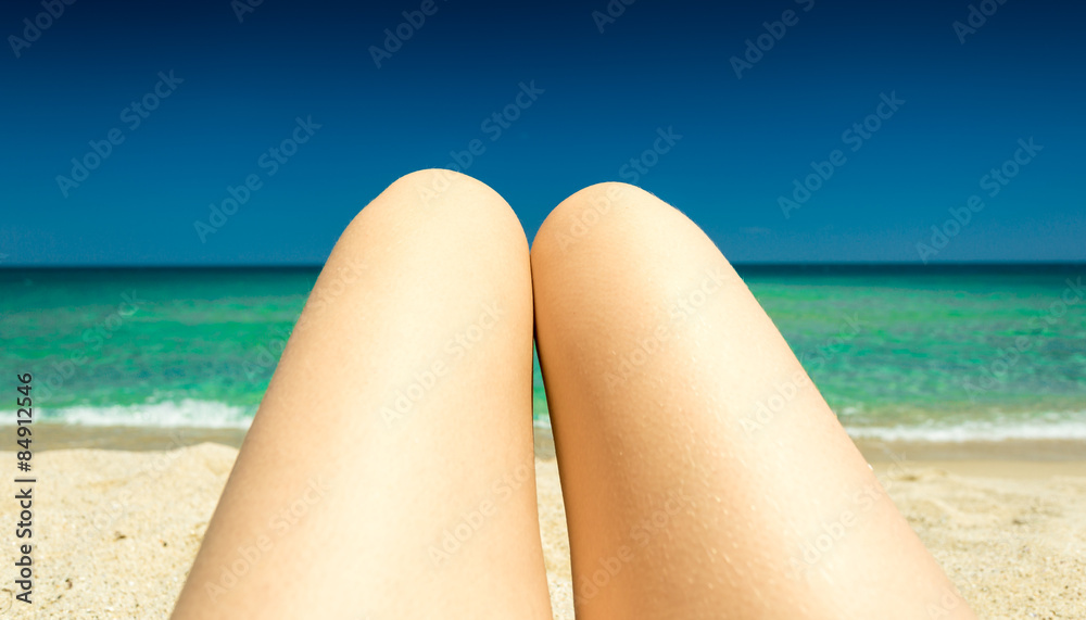 toned photo of slim female legs tanning on seashore toned photo of slim female legs tanning on seashore