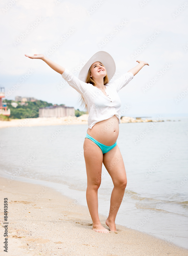 smiling pregnant woman standing on beach and holding hands up smiling pregnant woman standing on beach and holding hands up