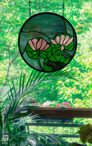 Water lily and frog Stain Glass picture in window looking out at deck and woods © vermontalm