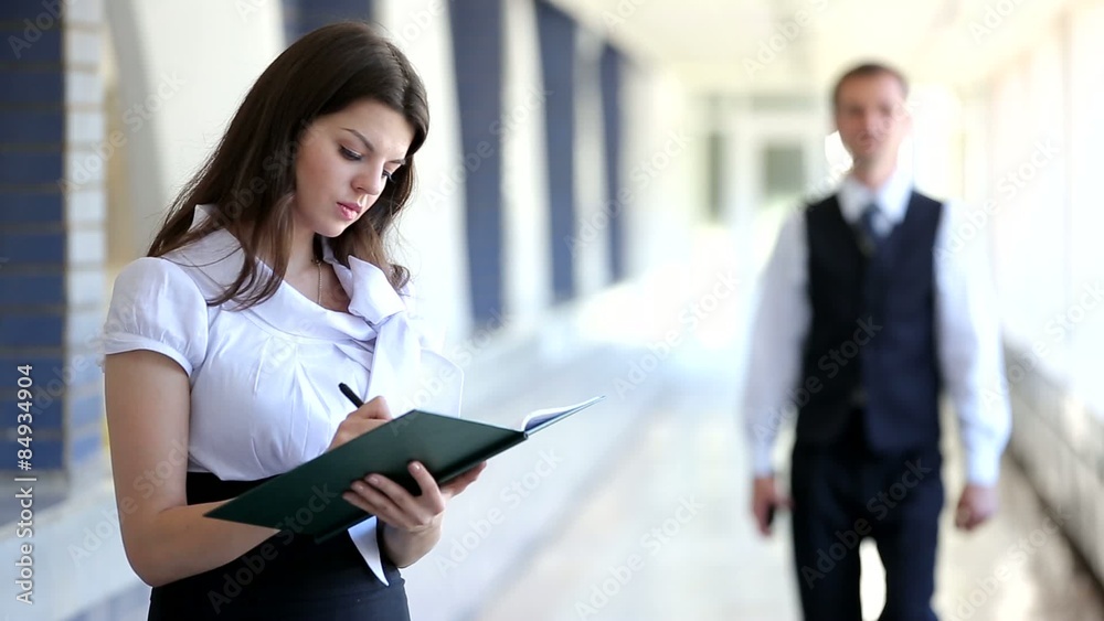 Business woman standing with a notebook, a businessman walking down the corridor Business woman standing with a notebook, a businessman walking down the corridor