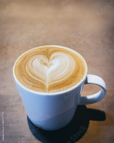 Cup of Coffee with heart pattern on wooden background