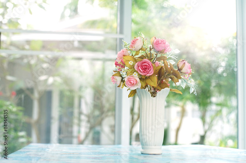 pink artificial roses in ceramic vase near window with morning light