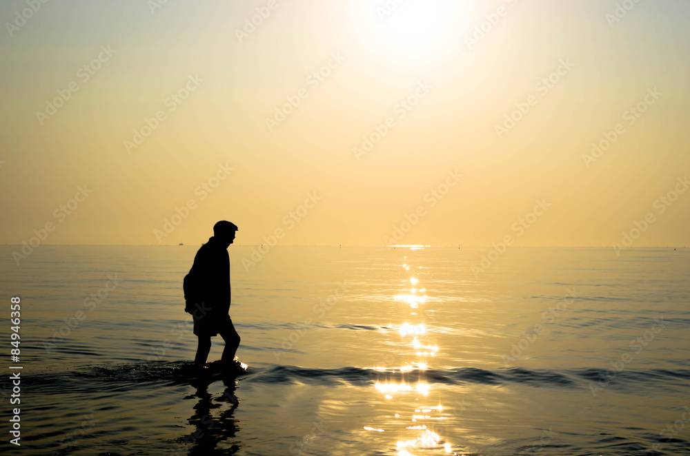 old man walking in the sea during sunrise - lifestyle concept