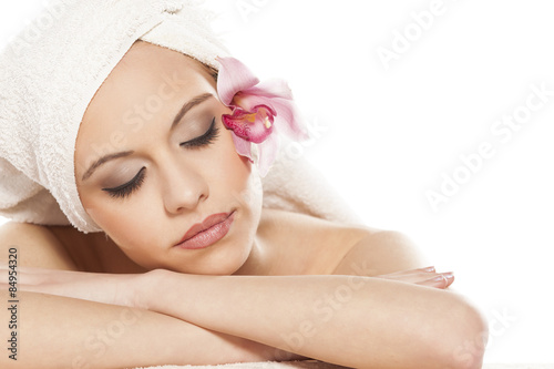 relaxed woman with orchid and towel on her head lying on white