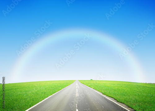 Road through the green field and sky with rainbow