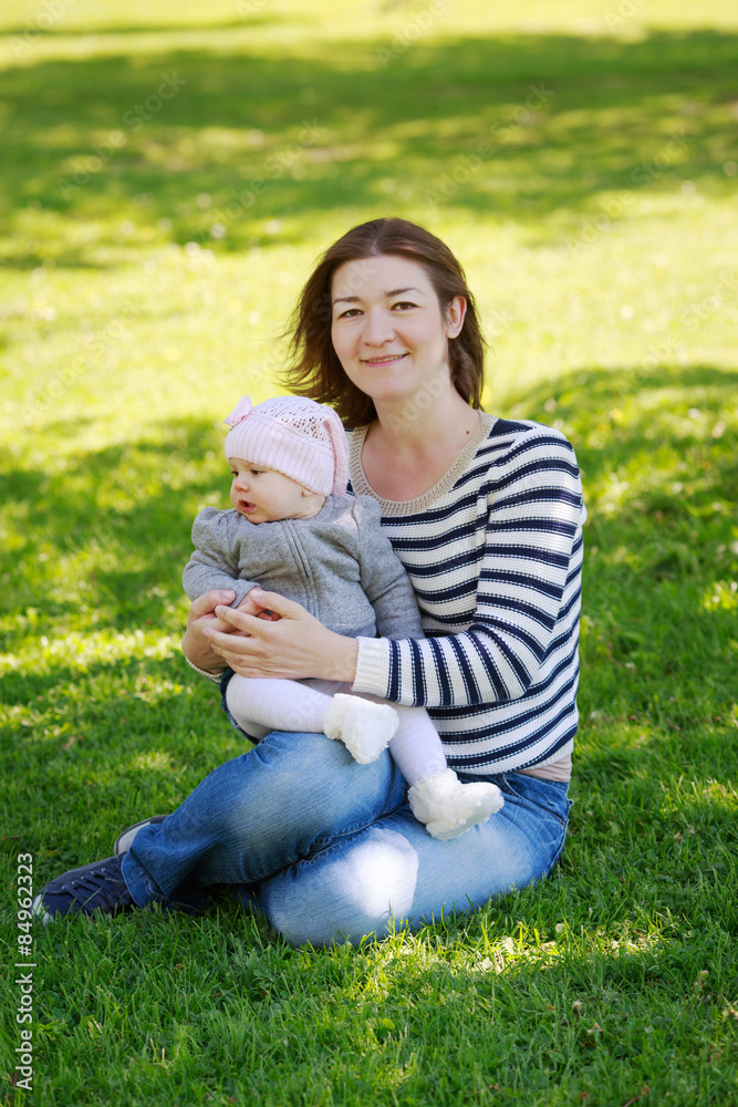 Fototapeta premium Portrait of mother and daughter, happy family of two, on the meadow in the park outside on a spring summer bright day, hugging, kissing and playing. Mothers Day
