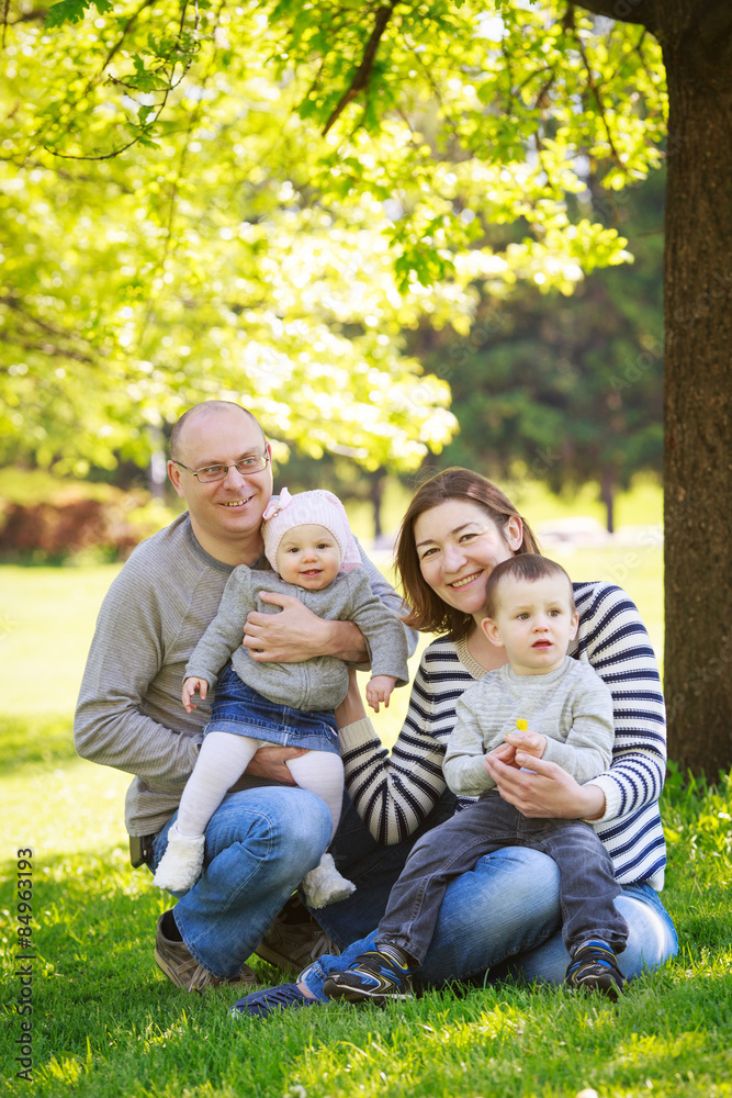 Portrait of mother, father, daughter and son, happy family of four, sitting on the meadow in the park outside on a spring summer bright day Portrait of mother, father, daughter and son, happy family of four, sitting on the meadow in the park outside on a spring summer bright day