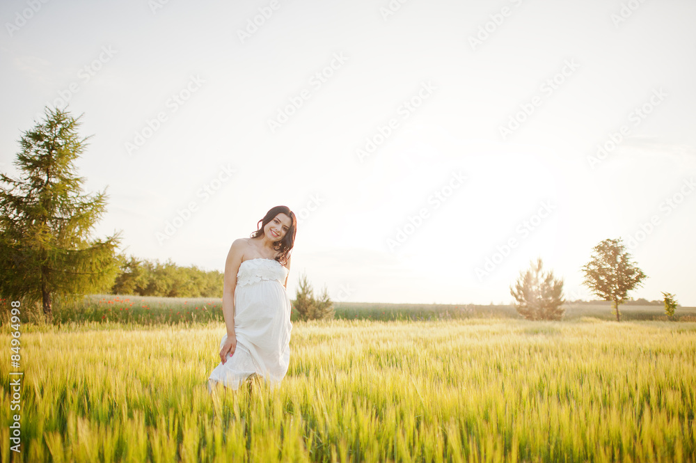pregnant gorgeous brunette woman on the field with wheat and pop