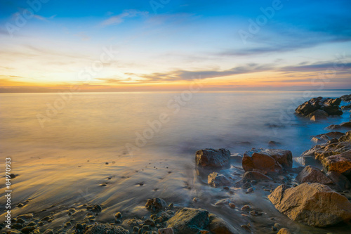 Sunset pours over coastal rocks and water elements of Soquel Cove in Capitola, California