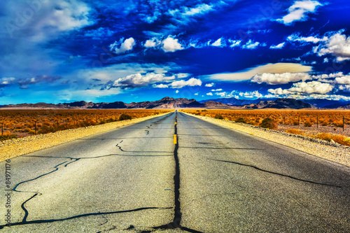 Tar lines of an open, desert highway as clouds dance on the horizon near Death Valley, California