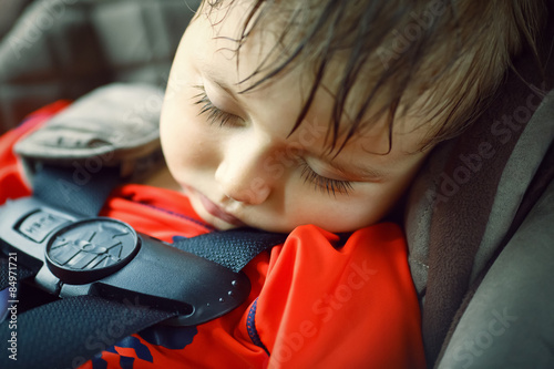 Closeup portrait of a cute adorable little boy toddler tired and sleeping belted in car seat on his trip, safety protection concept