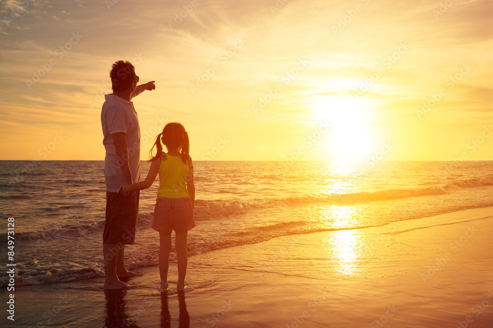 father and daughter standing on the beach watching sunset