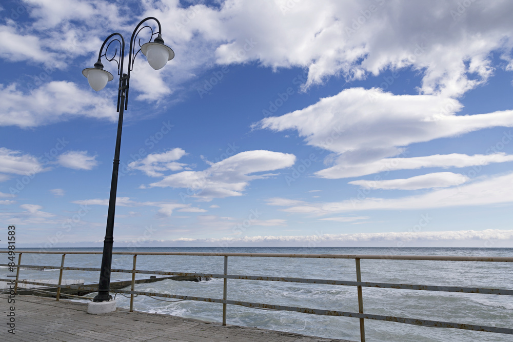 Lantern on the seafront against the sky with clouds.