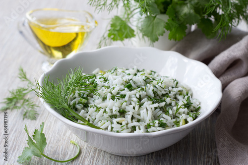 Rice with greens in a white bowl on a wooden table