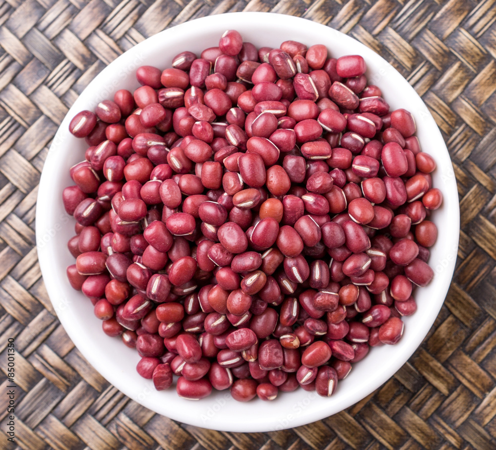 Red adzuki beans in white bowl over wicker background Red adzuki beans in white bowl over wicker background