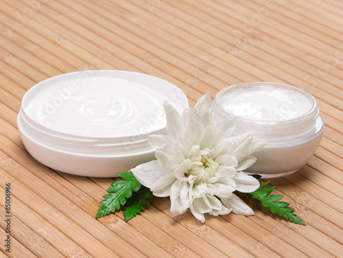 Fototapeta Naklejka Na Ścianę i Meble -  Open jars of cream with white flower and fern leaves