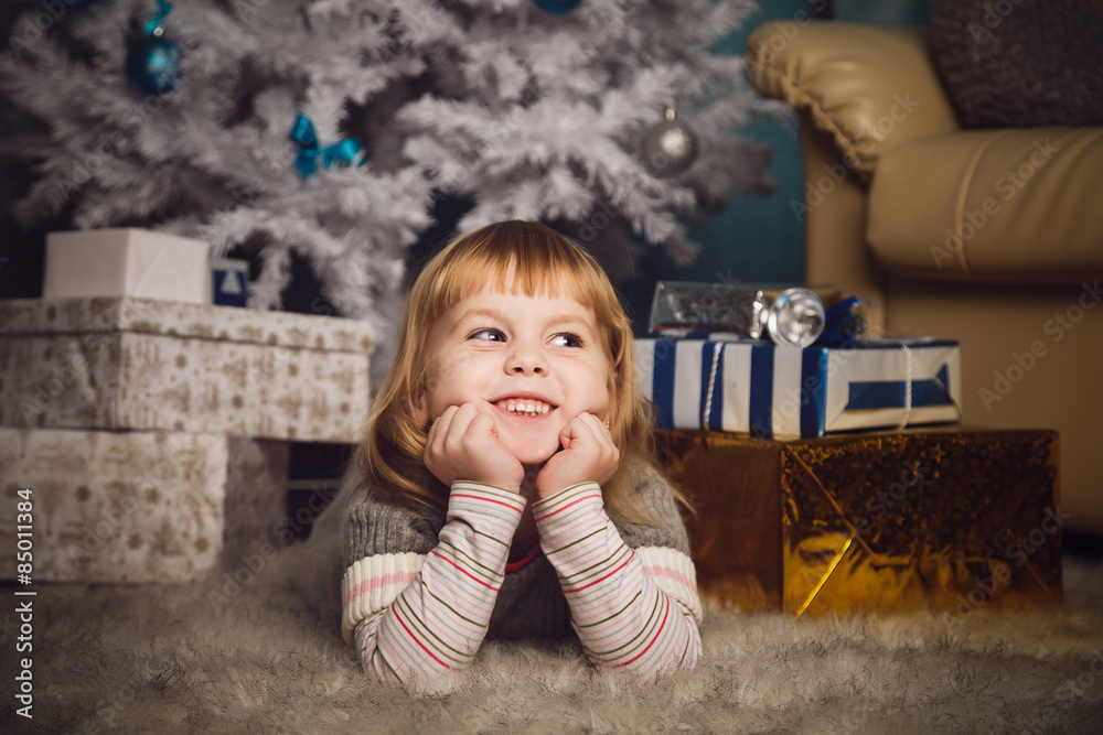 Naklejka premium Little girl lying near the christmas tree