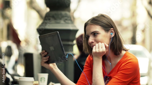 Young woman watching movie on tablet computer sitting in cafe in city
