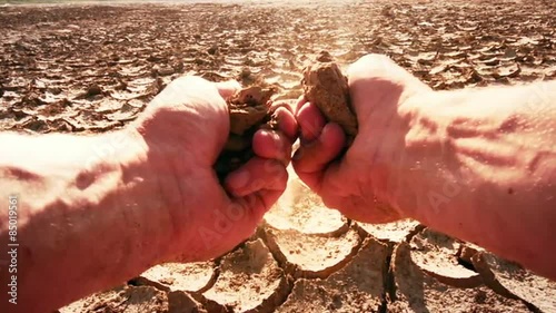 Farmer's hands split piece of dry soil from field affected by drought. Slow-mo