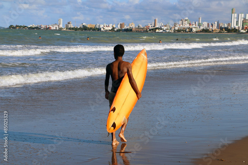 Brasilian young man walking with surfboard under his arm looking for a wave in Joao Pessoa
