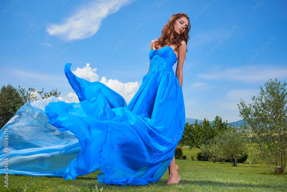 Fashionable beautiful young woman in long blue dress posing with