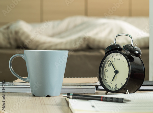 Cup mug and  retro alarm clock on the table in bedroom.