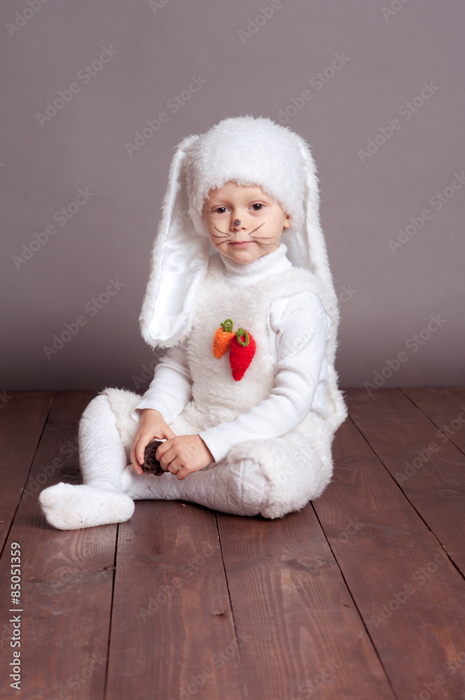 Obraz premium Smiling baby boy 3-4 year old sitting on wooden floor in room. Childhood. Wearing hare costume.
