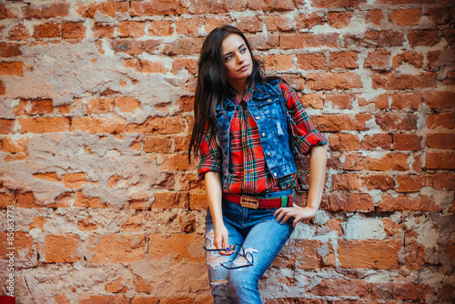 Beautiful young woman stands near the old brick wall. Youth styl