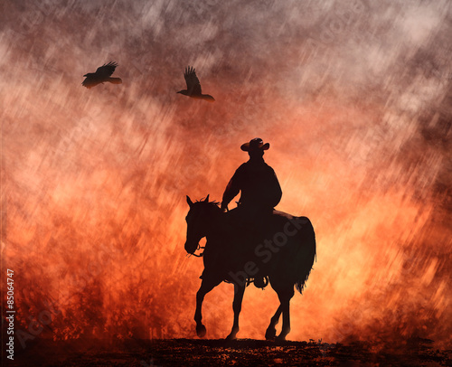 A cowboy on a horse riding into red fire with crows flying above. #85064747