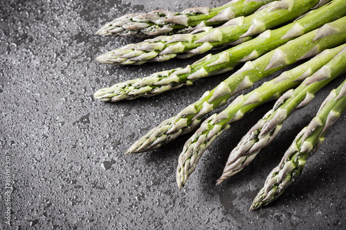 Fresh, wet asparagus on black surface.