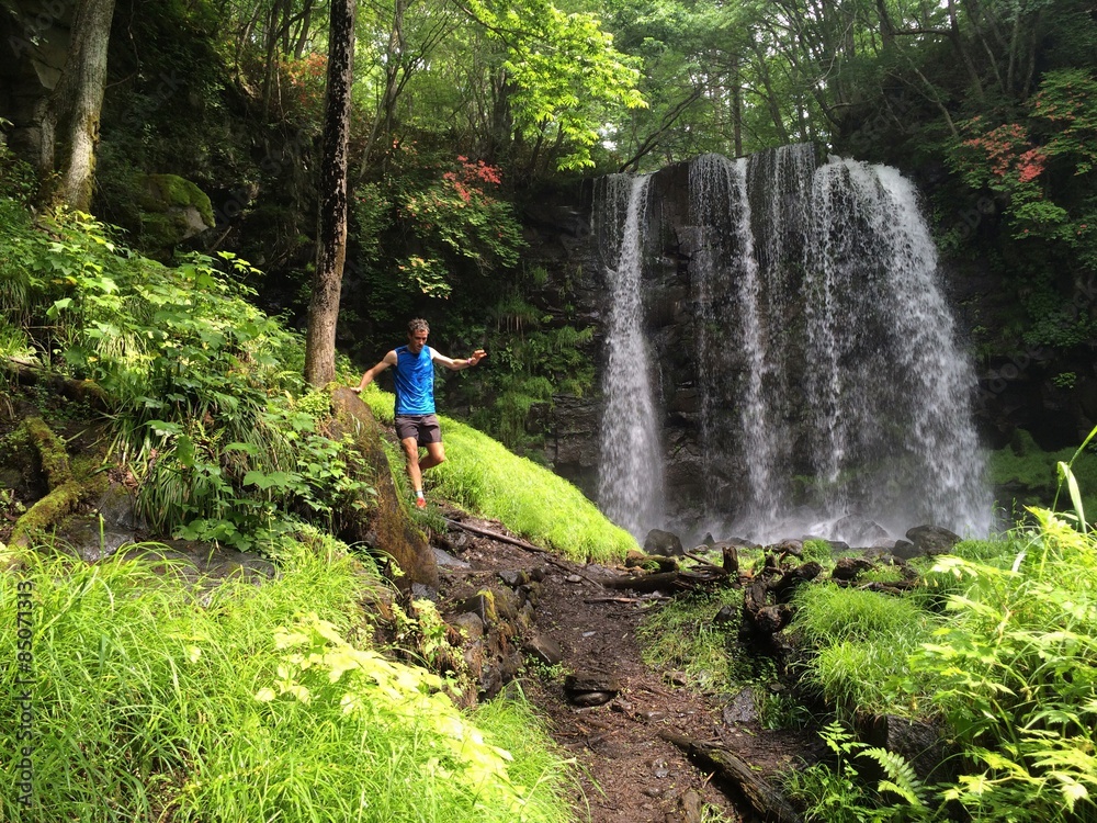 Fototapeta premium Runner on forest trail with waterfall behind
