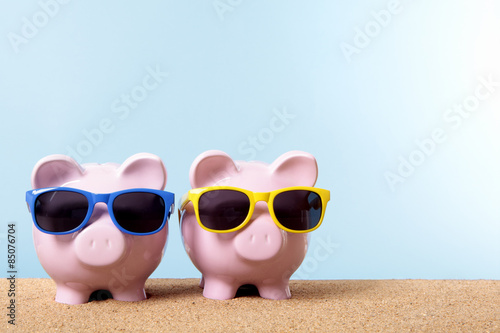 Two piggy Bank or piggybank wearing sunglasses standing on a sunny tropical beach holiday vacation retirement saving money plan photo