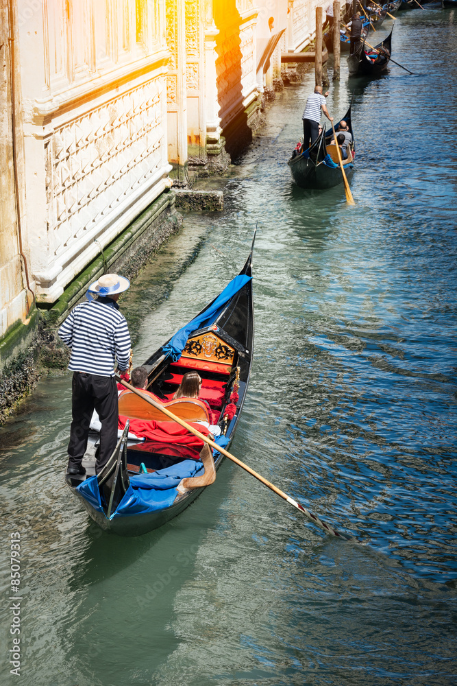 Venetian gondolier punting gondola through green canal waters of Venice Italy