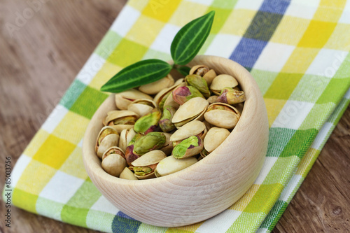 Pistachio nuts in wooden bowl on checkered cloth 