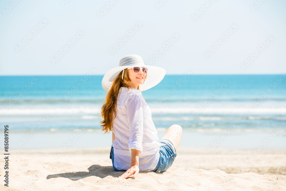 Beautifil young woman sitting on the beach at sunny day enjoing