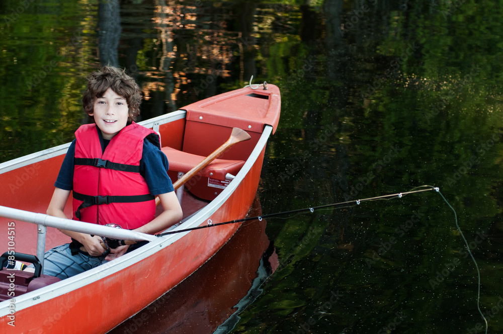 boy wearing a life-jacket fishing in a canoe