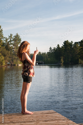 girl using her phone to take a picture of a sunset over a lake
