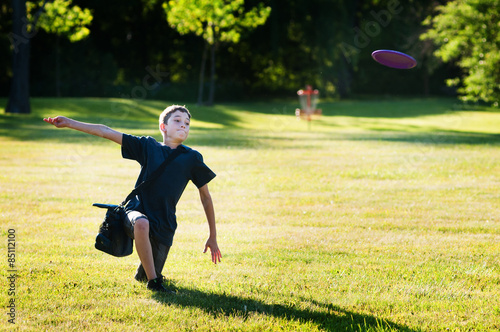 young boy playing disc golf in a park