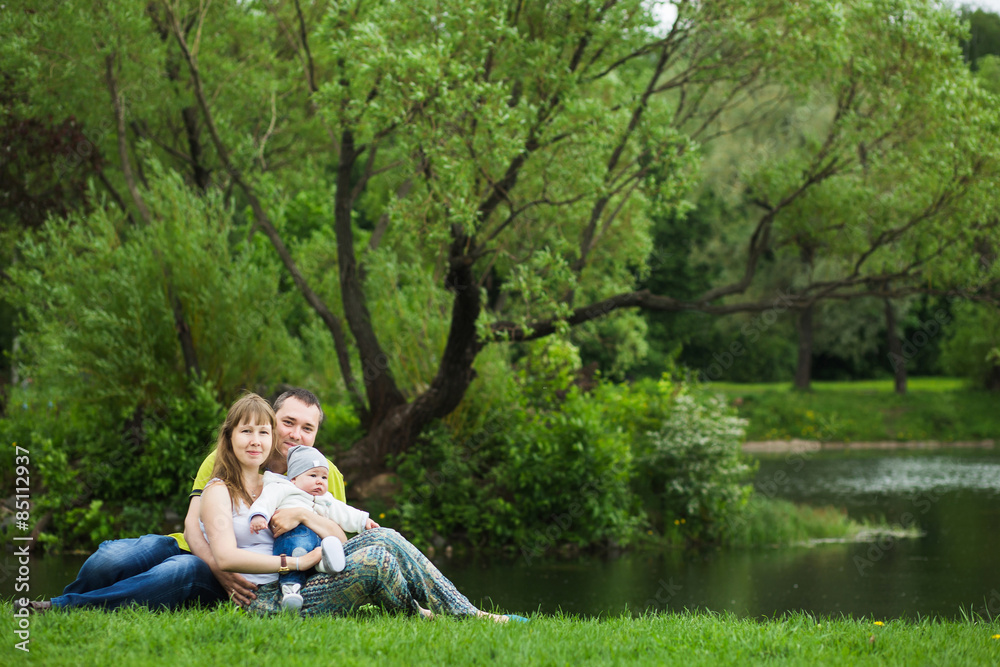 Happy family with a baby resting in summer park on the lake Happy family with a baby resting in summer park on the lake